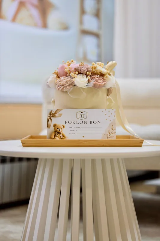 Poklon-bon Baby Spa Lu uz cvjetnu dekoraciju na stoliću.