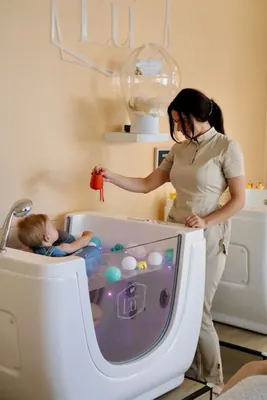 Odrasla osoba drži igračku iznad bebe u kolutu u kadici.